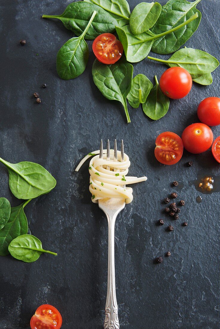 Linguine on a fork on a marble table, with tomatoes and spinach leaves