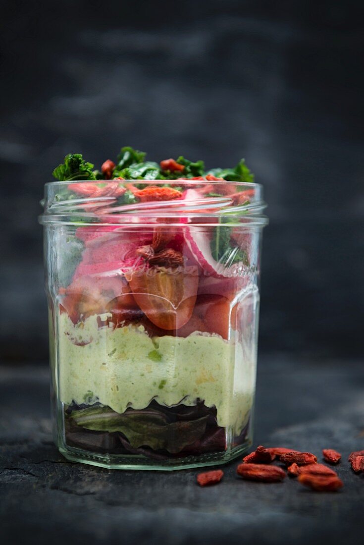 Mixed leaf salad with avocado, tomato, radish, cabbage, goji and vegan mayo in a glass jar