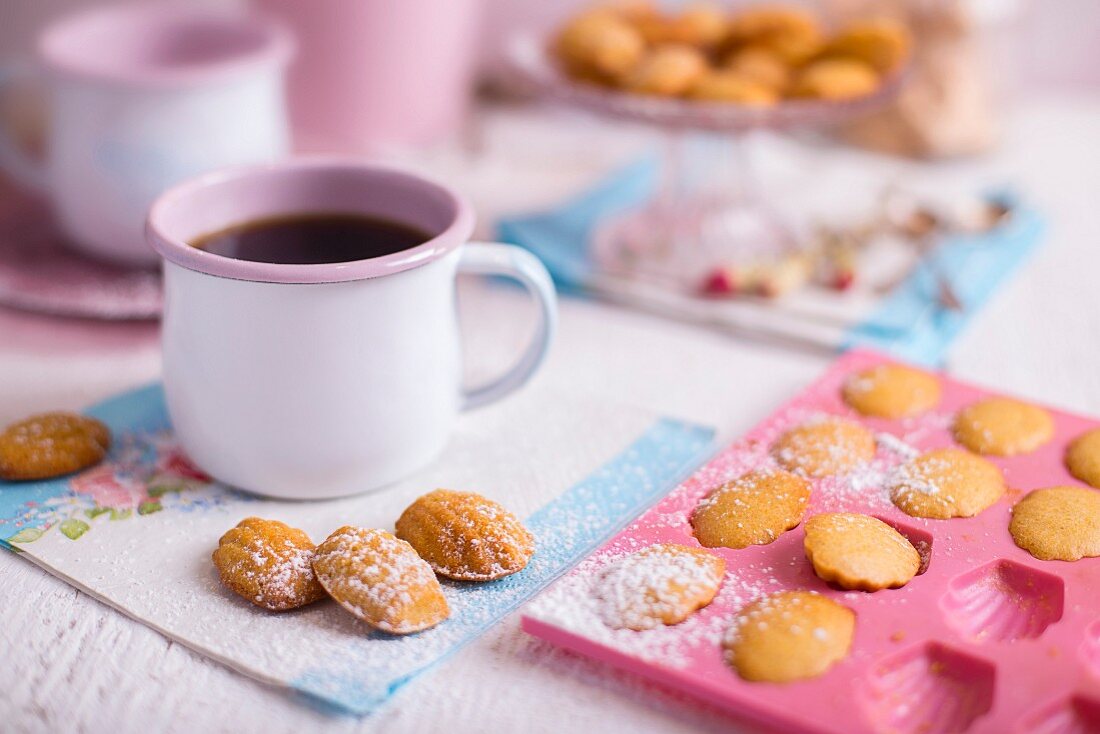 French Madeleines on a white wooden table with blue and pink decorations and a cup of coffee