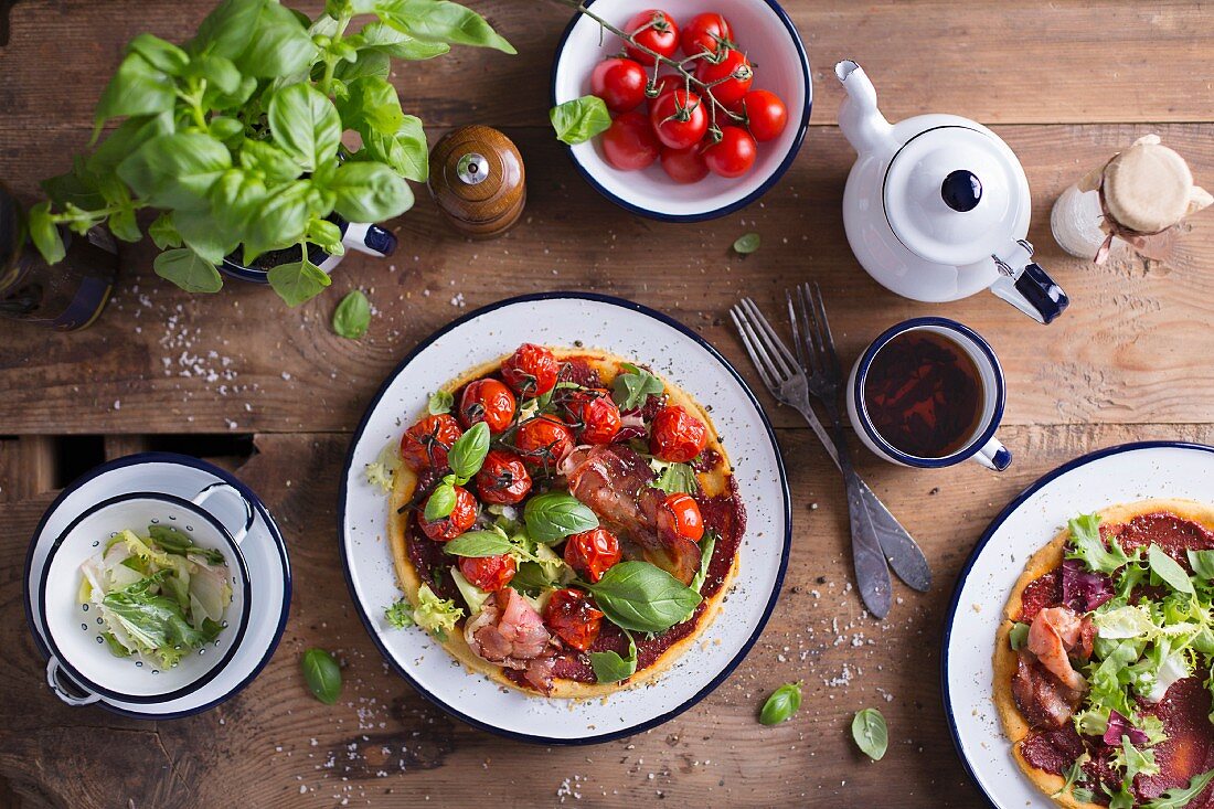 Gluten Free Pizza With Parma Ham, Fresh Basil Leaves And Cherry Tomatoes served on an enamel plate, on a wooden table