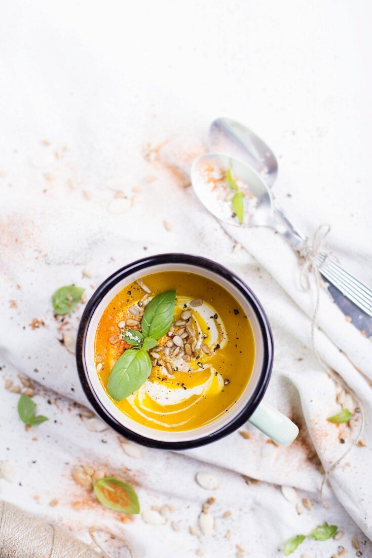 Pumpkin Soup in an enamel mug; decorated with fresh basil and sunflower seeds