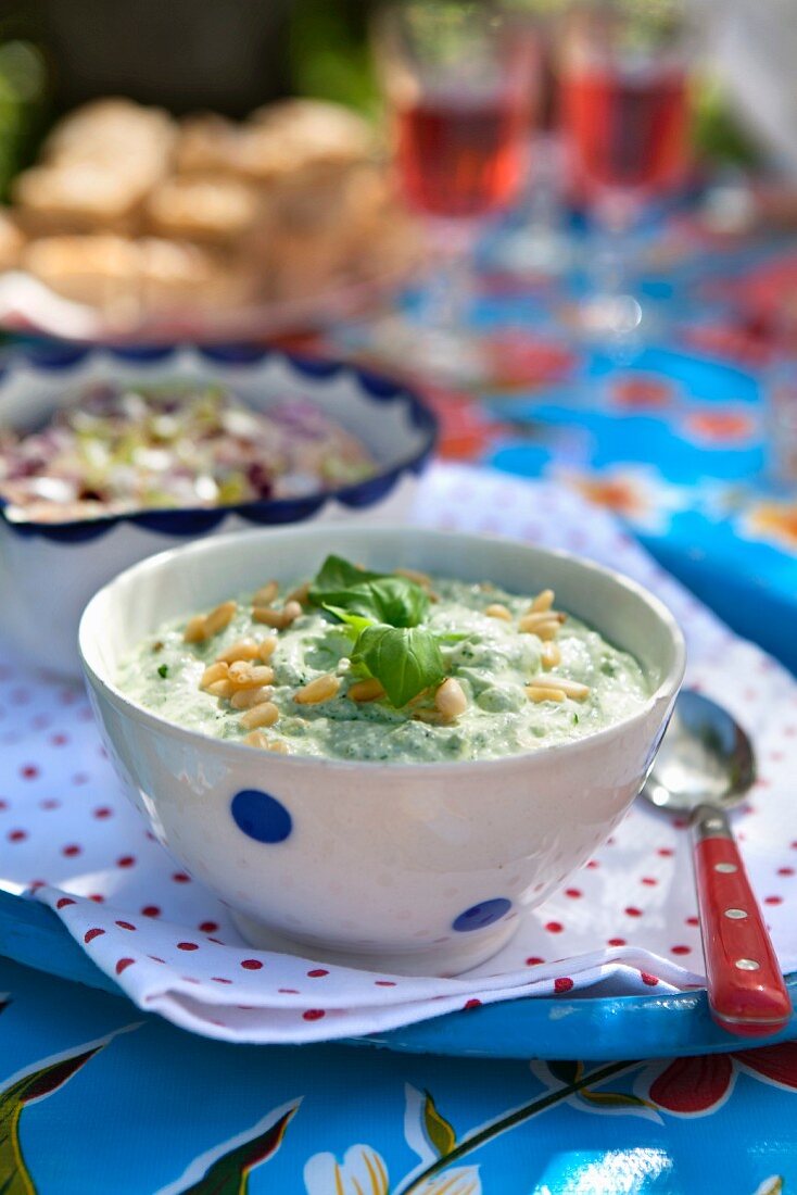 Cold basil soup with parmesan and pine nuts on a summer table outdoors