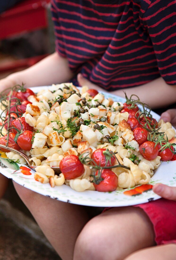 A pasta salad with grilled cherry tomatoes and halloumi on a serving platter