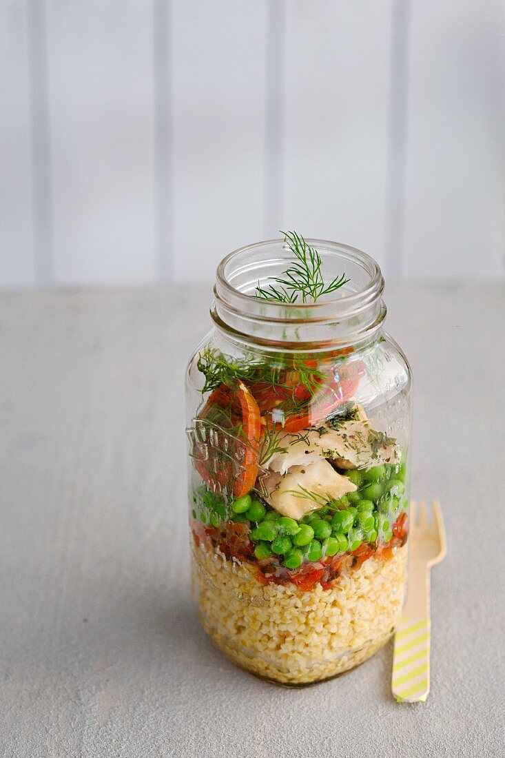 Couscous salad with fish, peas and tomatoes in a glass jar