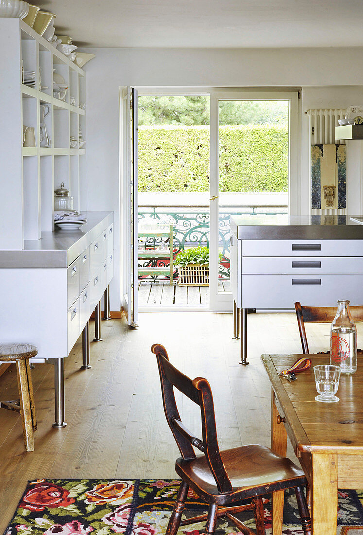 Rustic wooden table and white dresser with open shelves in the kitchen and view through open doors onto balcony