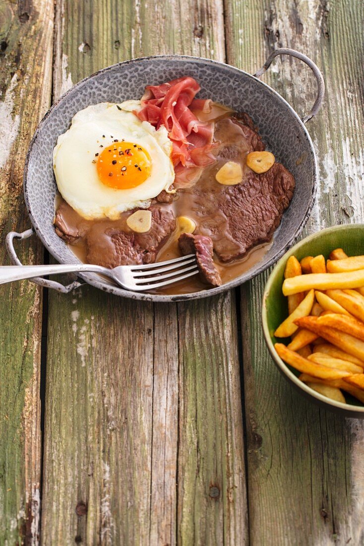 Steak in garlic sauce with a fried egg, ham and french fries