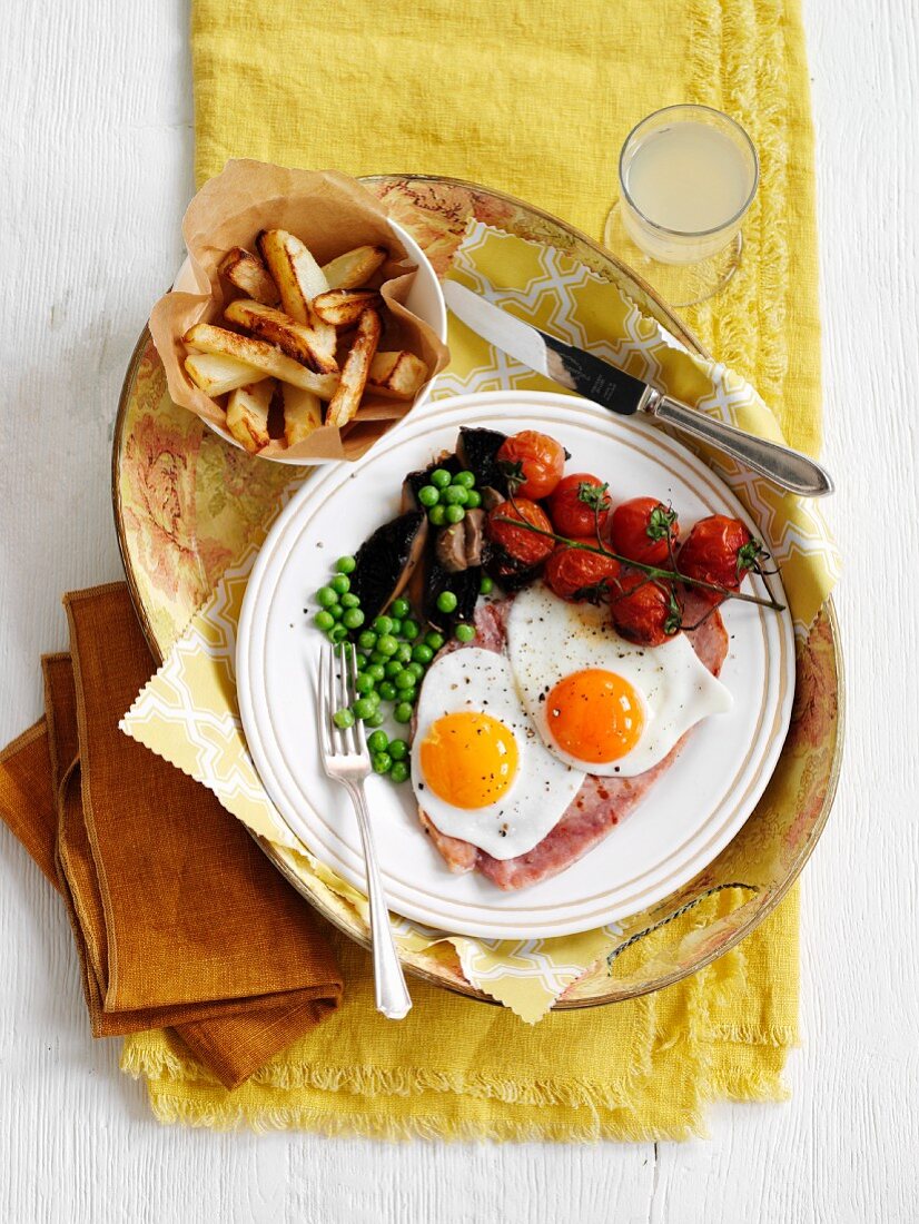 Grilled ham with fried eggs, peas, tomatoes and fries