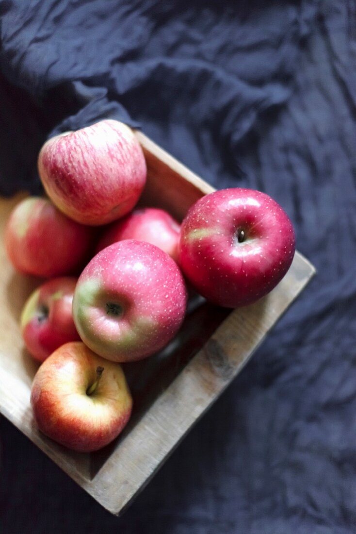 Pink apples in a wooden box on a dark grey fabric