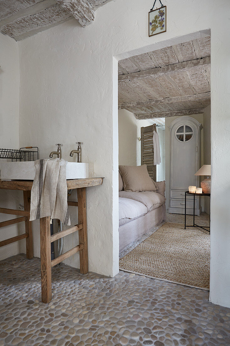 View through open doorway next to rustic wooden table with sink into living room with couch