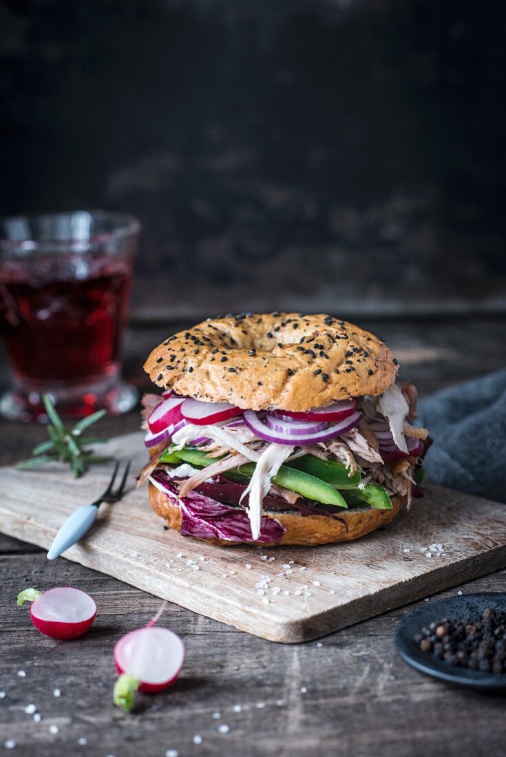 Dinkelbagel mit schwarzem Sesam, Radieschen, grüner Paprika, roter Zwiebel und Pulled Chicken