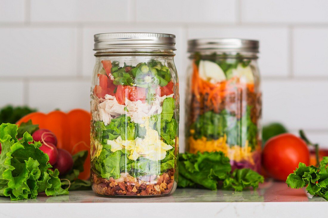 Two layered salads in glass jars with spinach, beans, cheese and eggs
