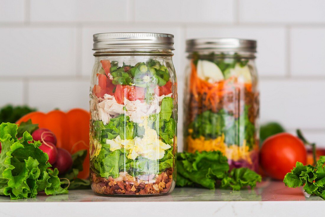 Zwei Schichtsalate im Glas mit Spinat, Bohnen, Käse und Ei