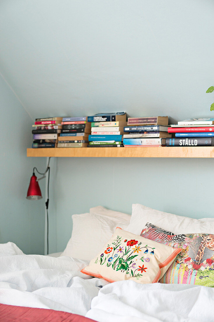 Books on shelf above bed under sloping ceiling