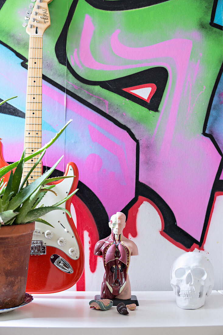 Anatomiemodell, Totenkopf und Gitarre vor Wand mit Graffiti