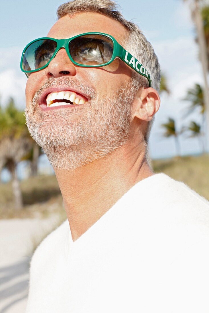 Mann mit grauen Haaren in weißem T-Shirt und grüner Sonnenbrille
