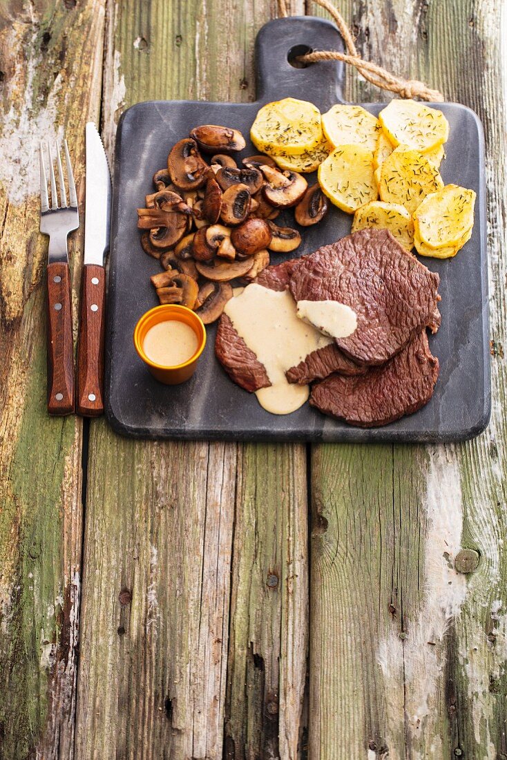 Grilled beef steaks with mushrooms, sauce and fried potatoes on a marble board