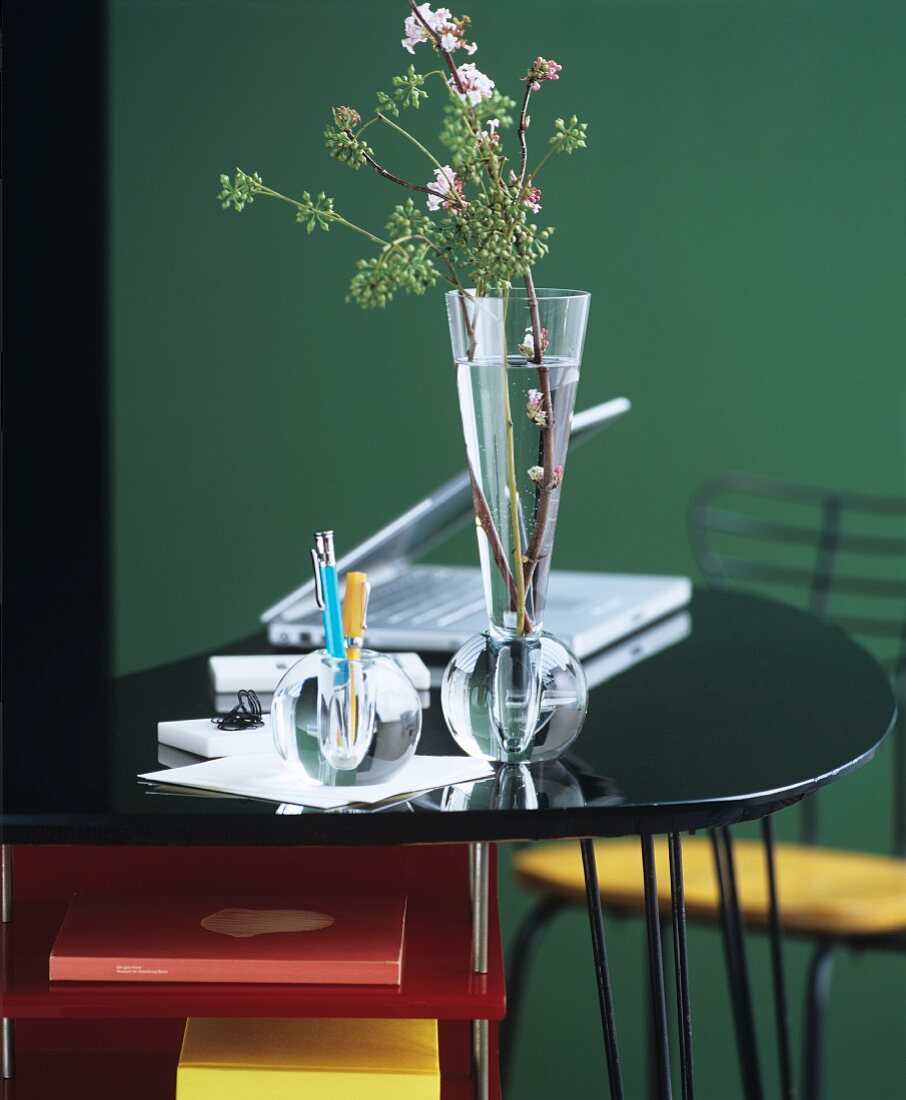 Glass vase and glass pen holders in front of green wall