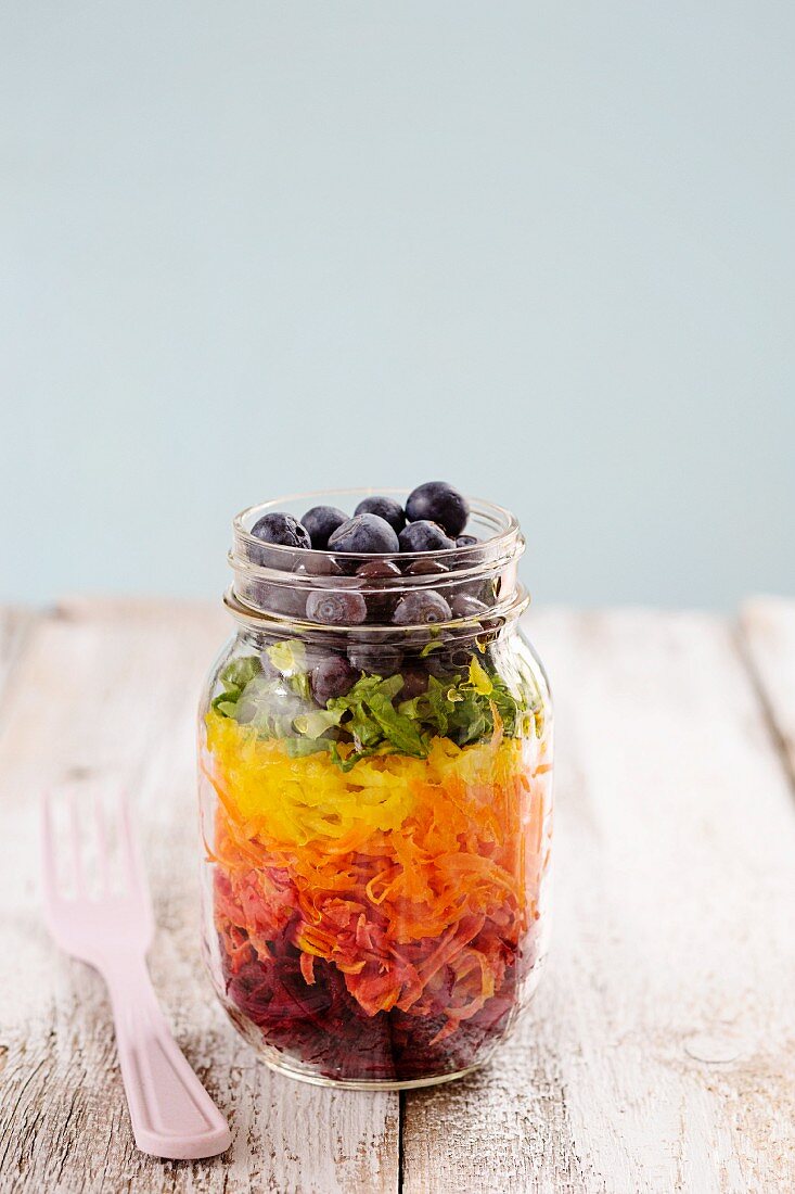 Rainbow salad in a glass with beetroot, carrots, yellow peppers, lettuce and blueberries