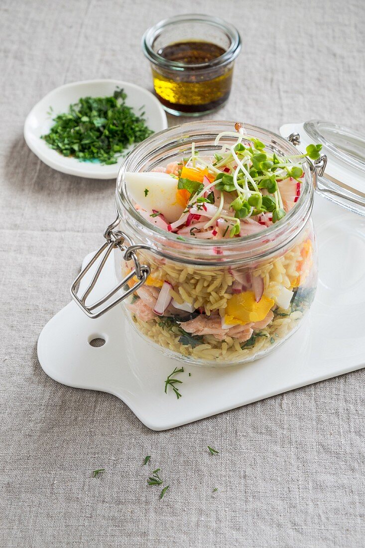 Wholegrain rice salad in a glass jar with salmon, boiled eggs, radishes and cress