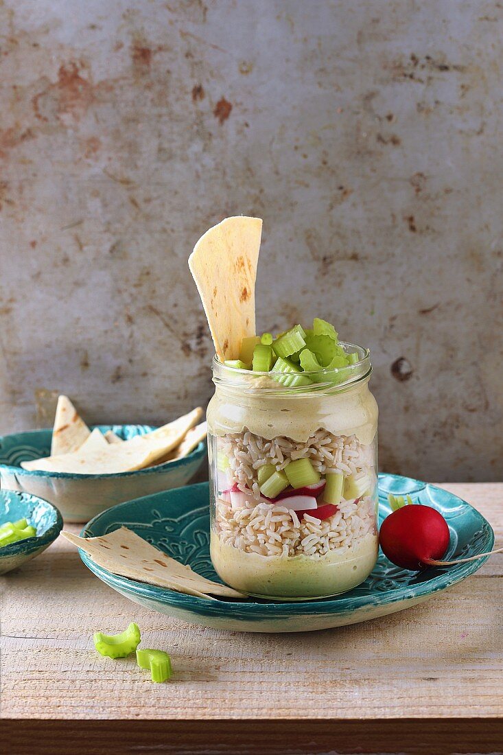 Brown rice salad with houmous, radish and celery in a glass jar