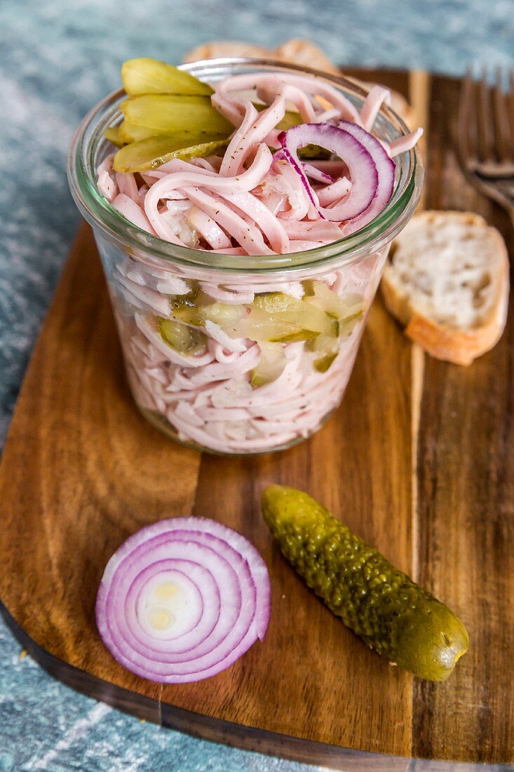 Sausage salad with red onion and gherkins in a glass on a wooden board