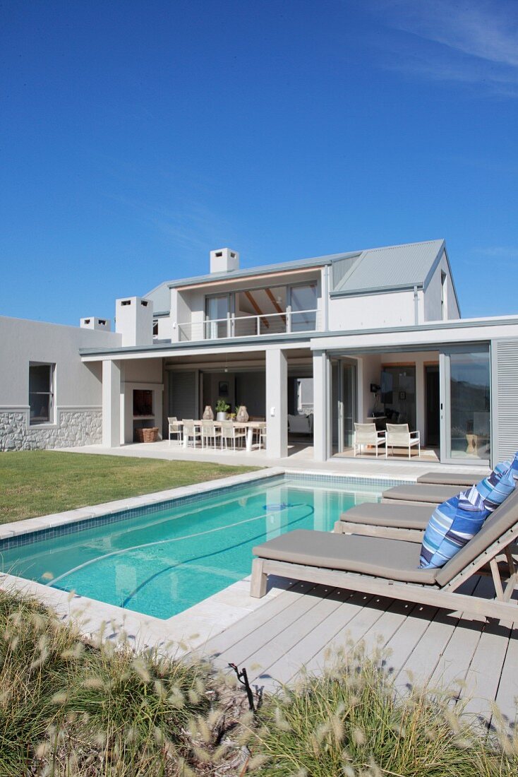 Blick auf elegantes Ferienhaus mit Pool und Rasenfläche unter blauem Himmel