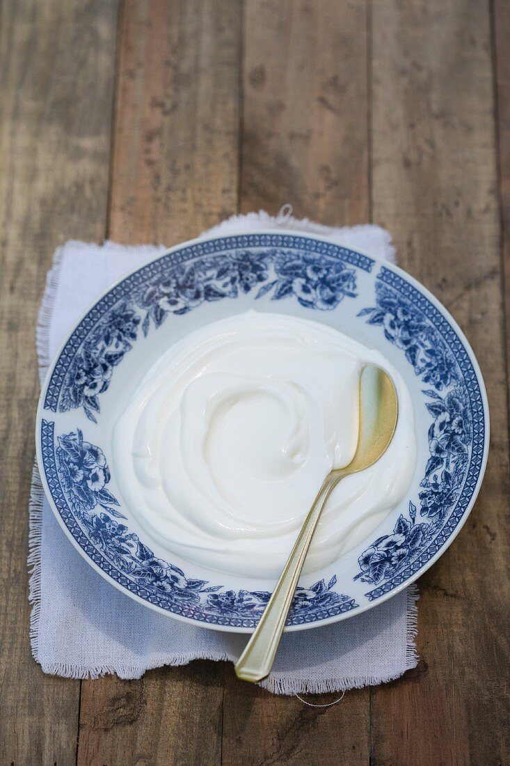 Naturjoghurt auf weiss-blauem Unterteller mit Teelöffel