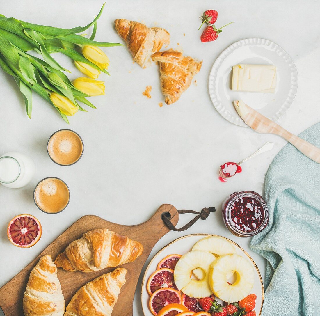Croissants, Butter, Marmelade, Obst, Espresso und Tulpen auf Frühstückstisch (Aufsicht)