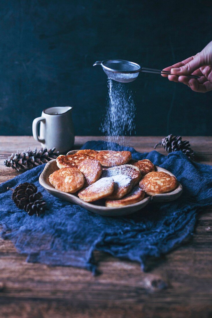 Woman s hand dusting sweet fritters with powdered sugar
