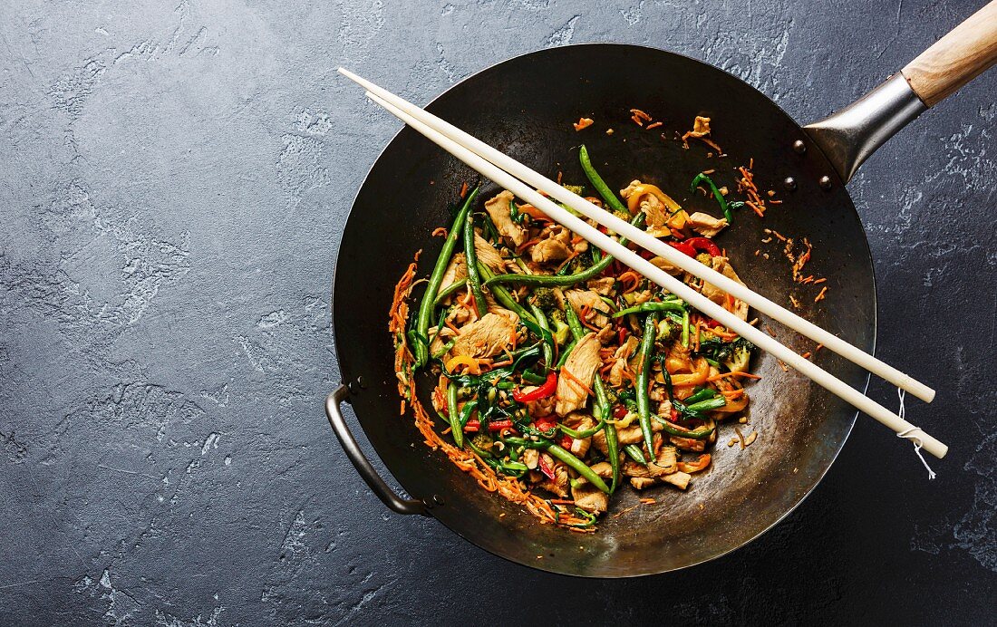 Stir fry chicken with sweet peppers and green beans in wok pan on dark stone background