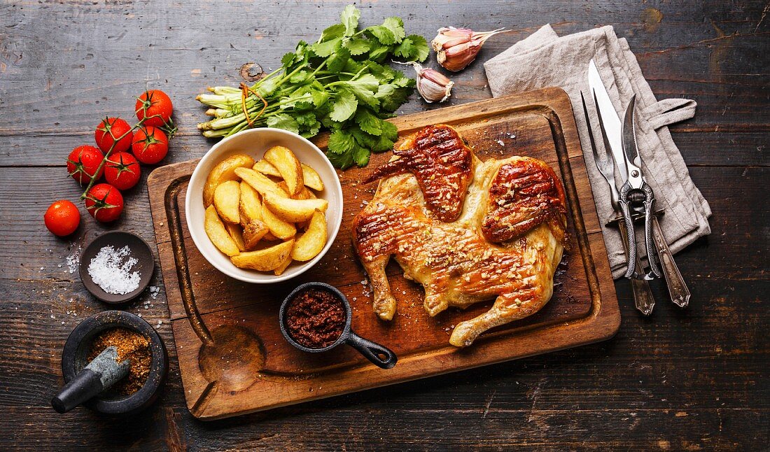 Chicken Tabaka (Pfannengebratenes Huhn, Georgien) mit Kartoffelspalten auf Holzbrett