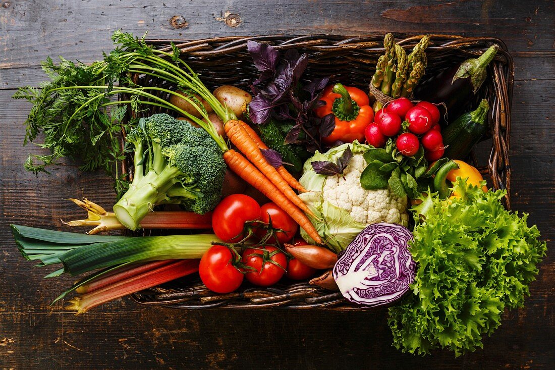 Fresh vegetables in basket on wooden background