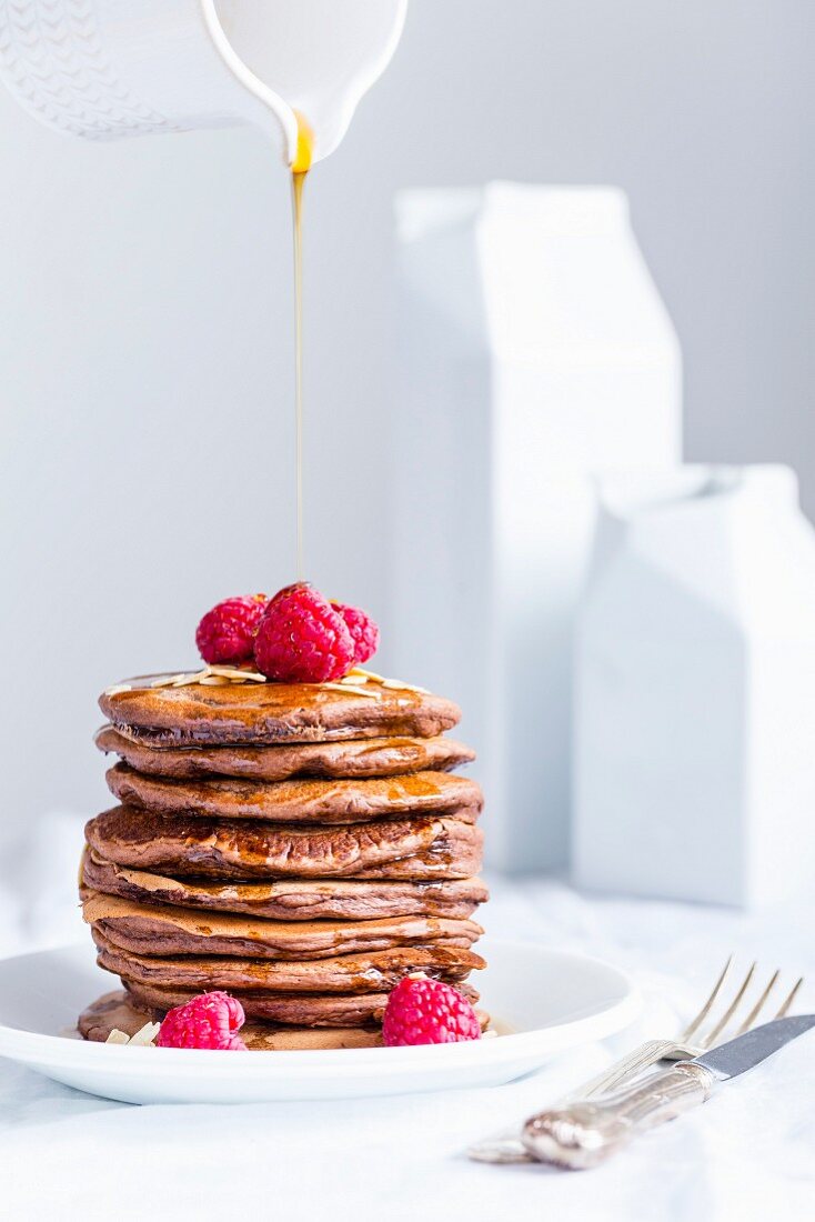 Stack of homemade american eggless chocolate pancakes with maple syrup flowing from jar