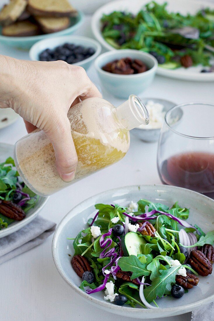 Hand pouring Toasted Walnut Sherry Feta Vinaigrette onto a Spicy Pecans Feta Arugula Salad