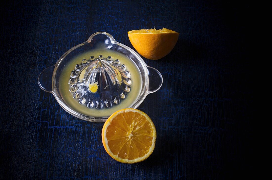 A halved orange with a juice press on a dark background