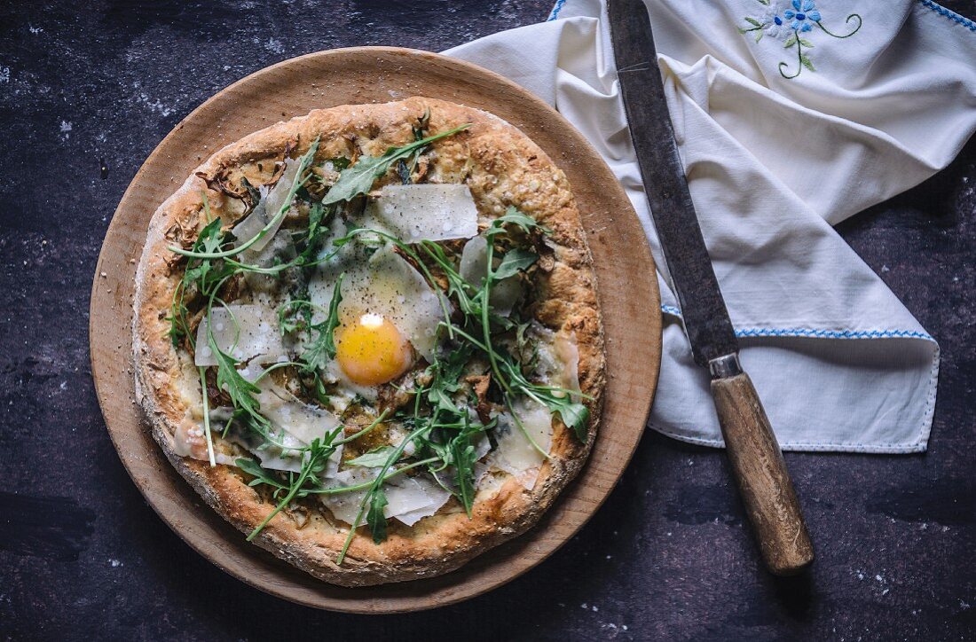 Pizza with fried egg, rocket and parmesan (top view)