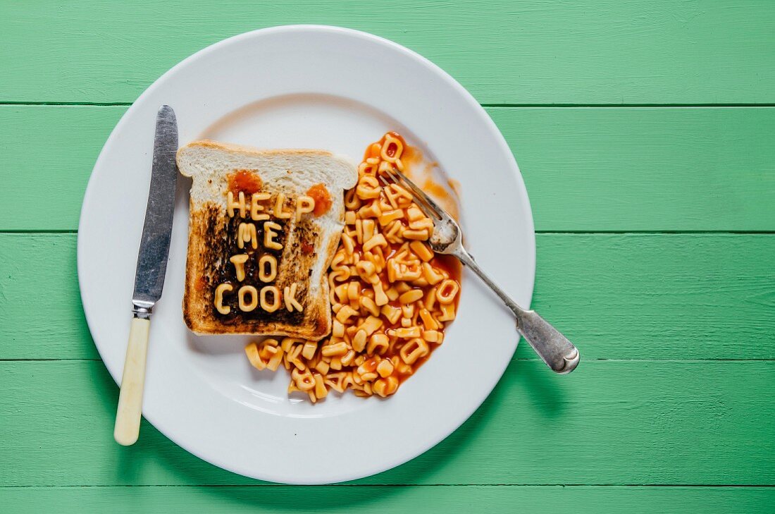 Verbrannter Toast mit Schriftzug 'Help me to cook' aus Buchstabennudeln