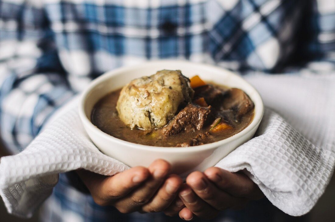 Hands holding a bowl of beef stew