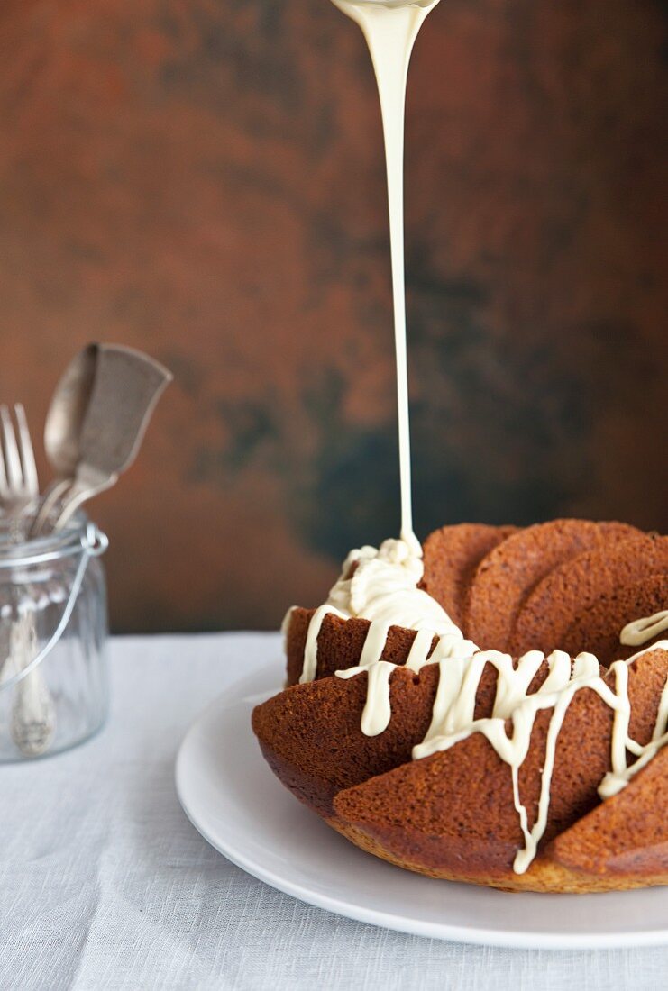 A ring-shaped Bundt cake being drizzled with white chocolate