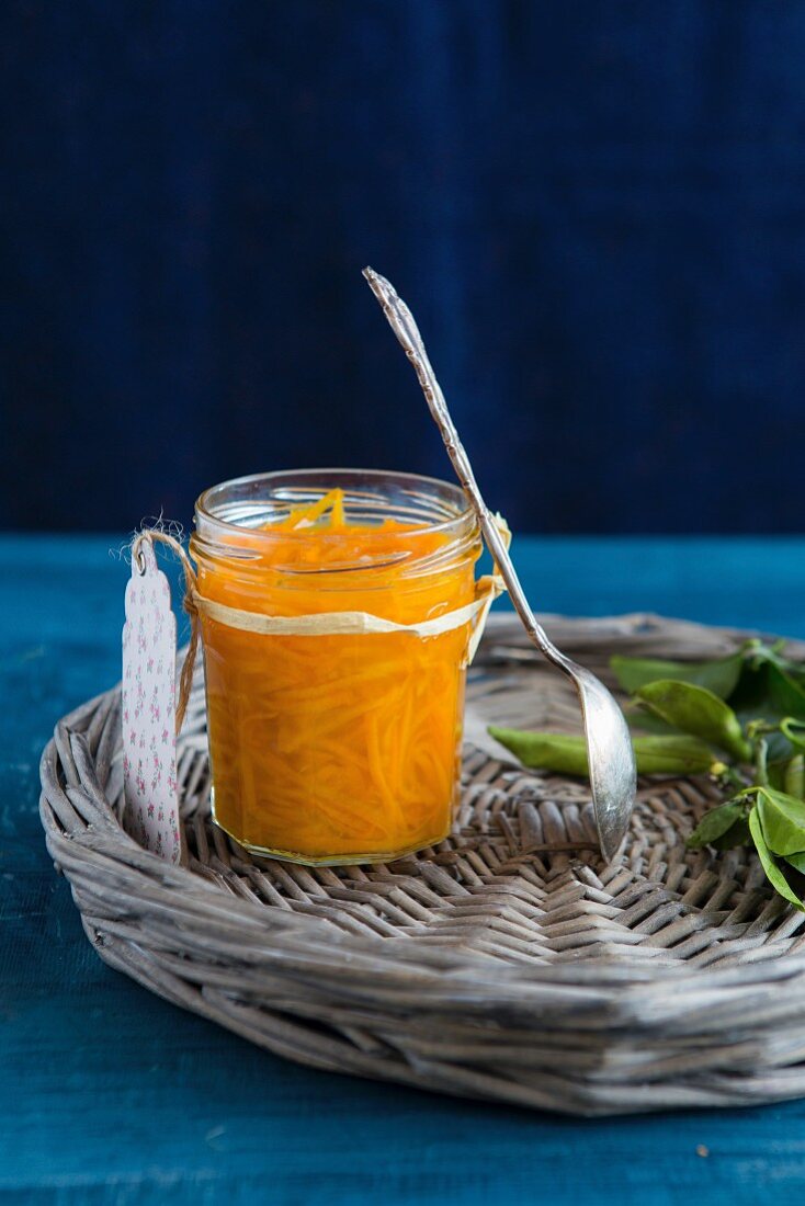 Orangenmarmelade im Glas mit angelehntem Löffel auf Korbtablett