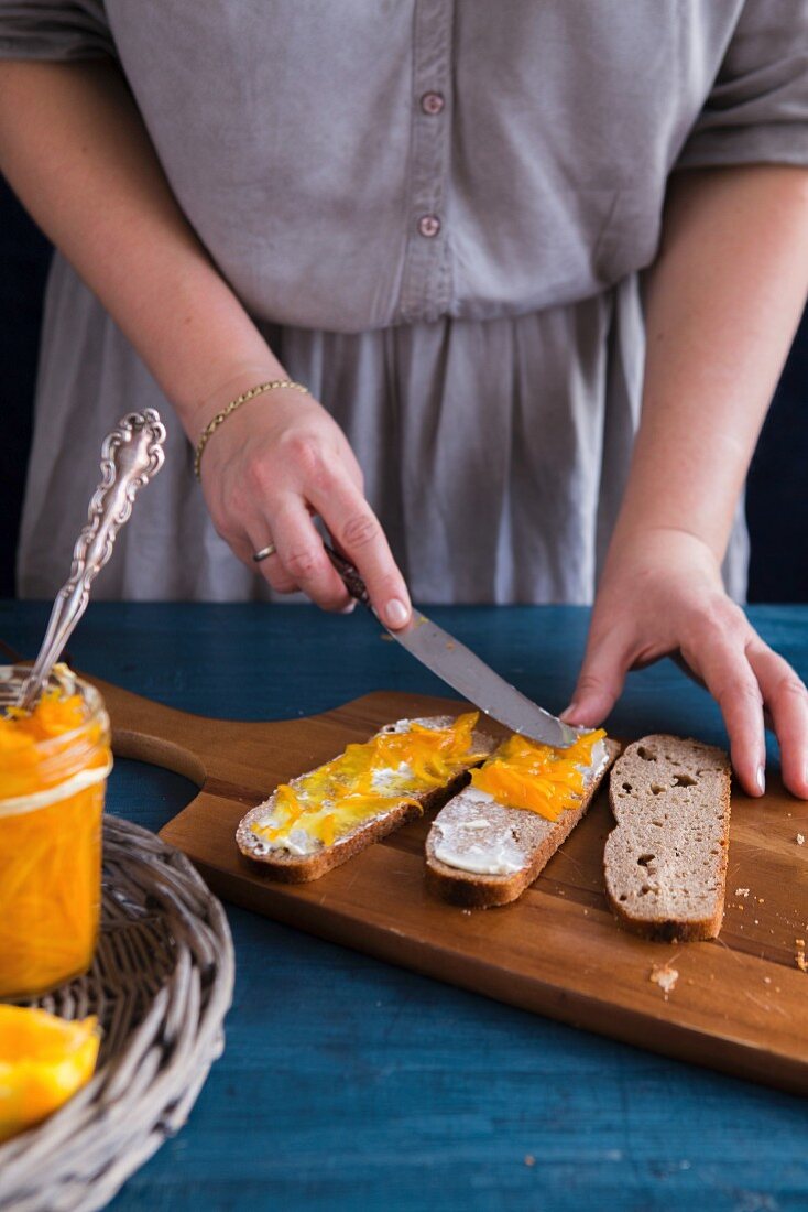 Frau streicht Orangenmarmelade auf Brot