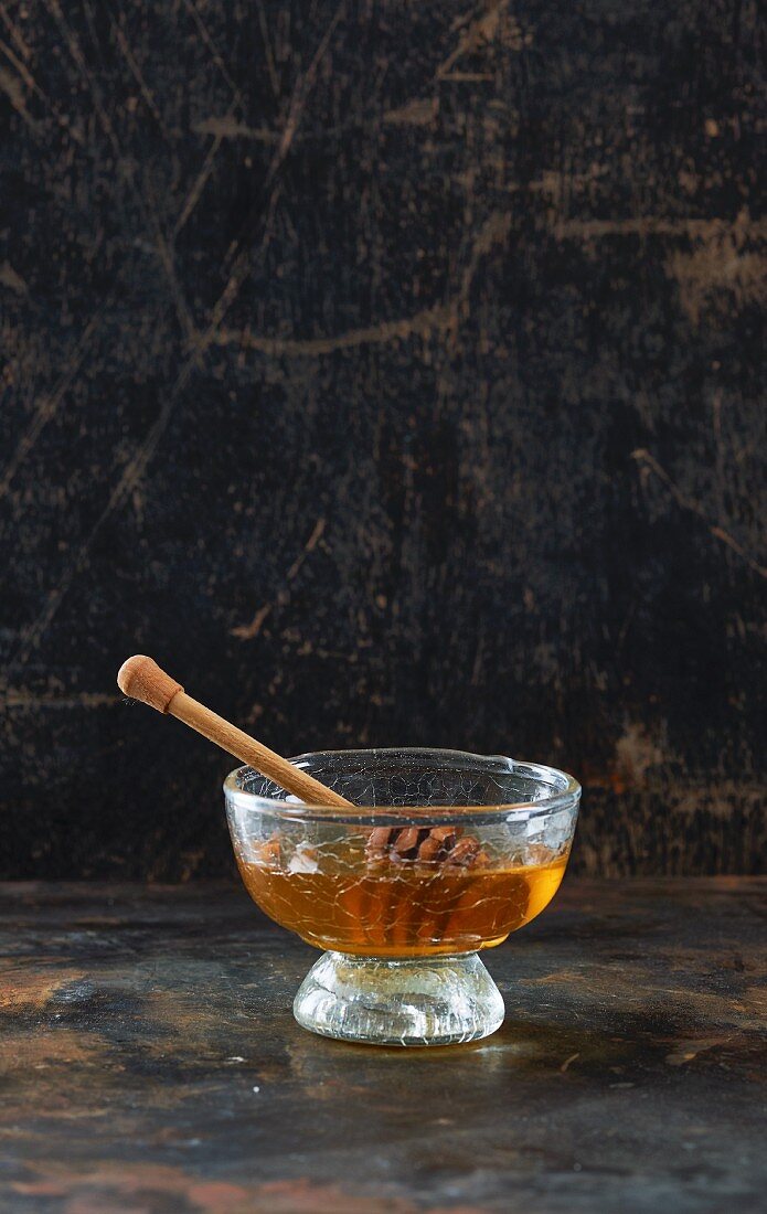 Honey with a honey spoon in a glass bowl in front of a dark background