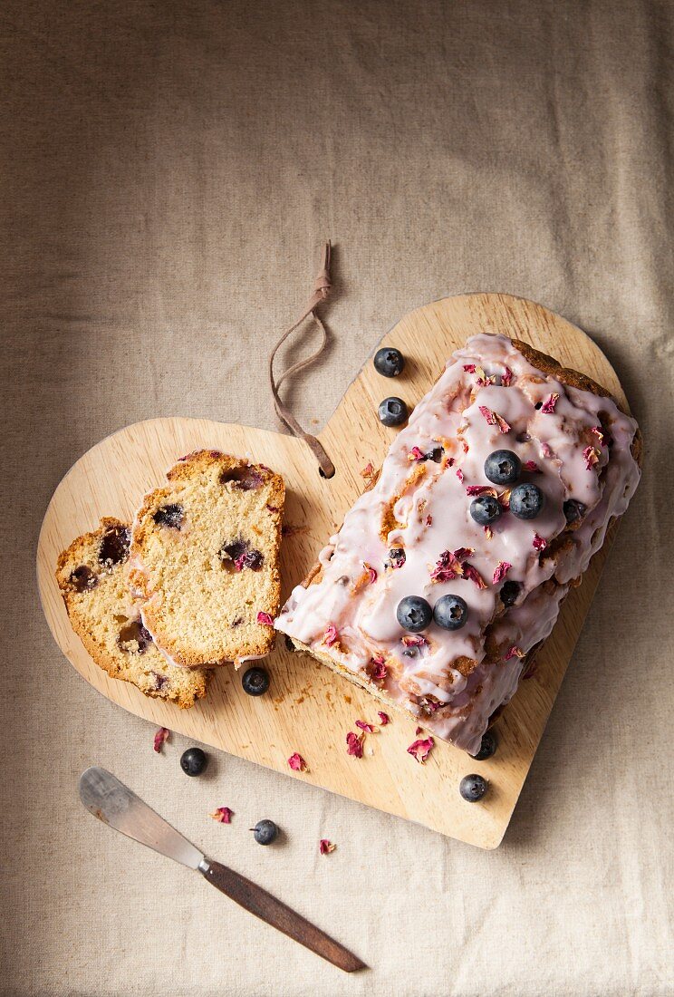 A sliced blueberry loaf cake with icing and dried rose petals