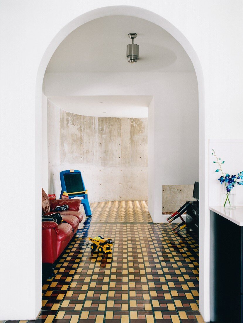 Red leather couch and curved concrete wall seen through white arched doorway