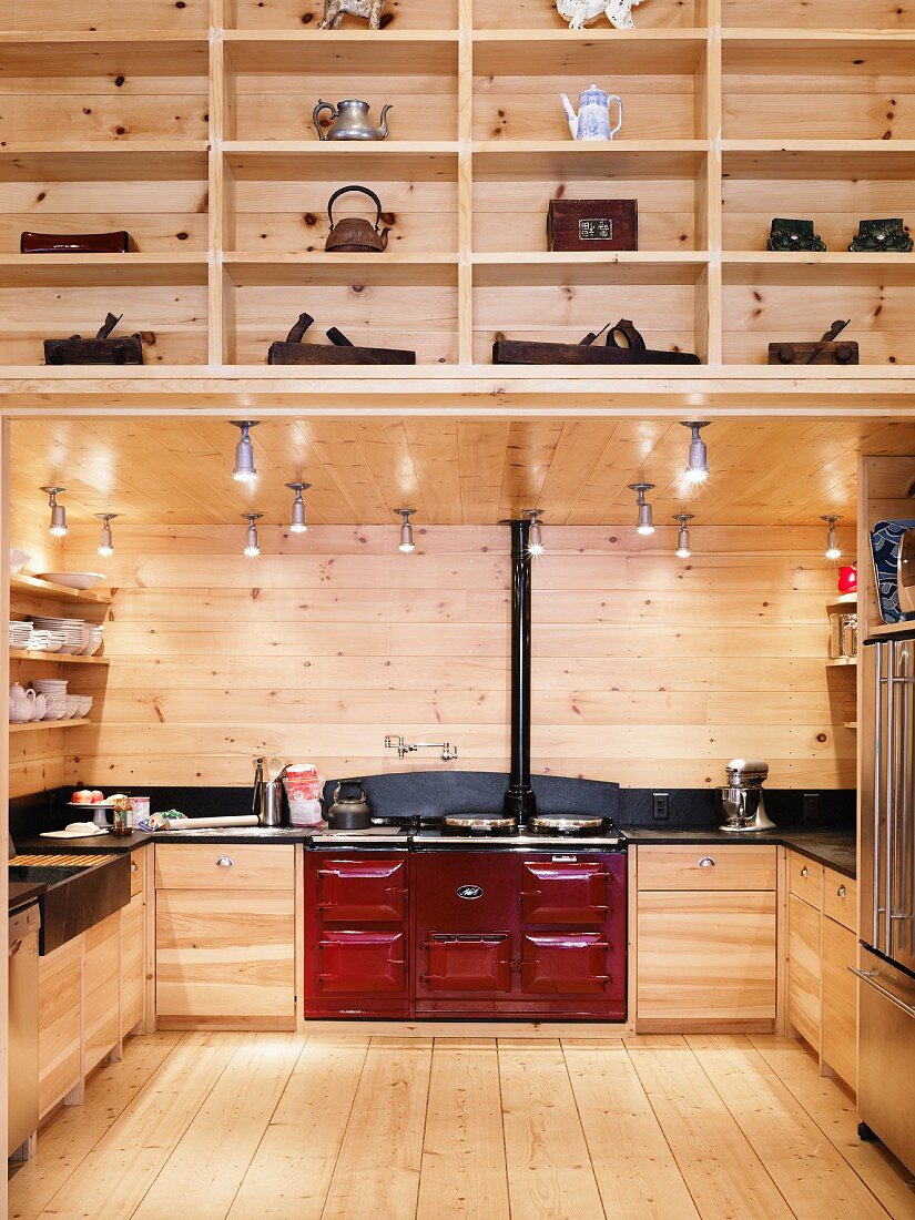 Illuminated fitted wooden kitchen with red AGA cooker in wooden house with fitted shelving in foreground