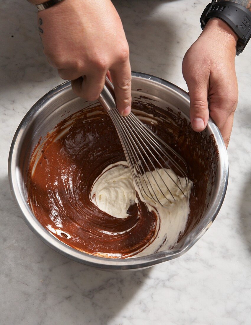 Cream being mixed into melted chocolate with a whisk in a metal bowl