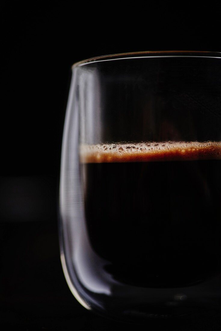 A cup of freshly brewed black coffee in front of a black background