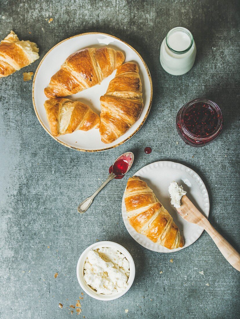 Freshly baked croissants with raspberry jam, cream cheese and milk in bottle over grey concrete background