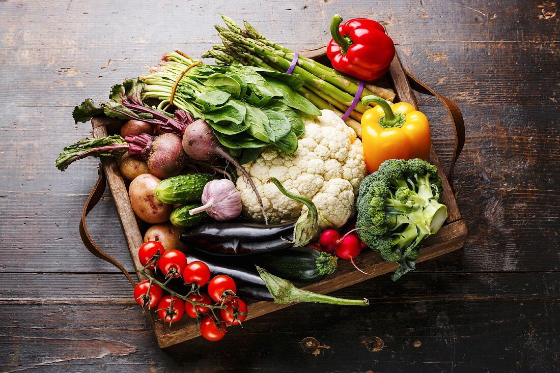 Fresh raw vegetables in wooden box on wooden background