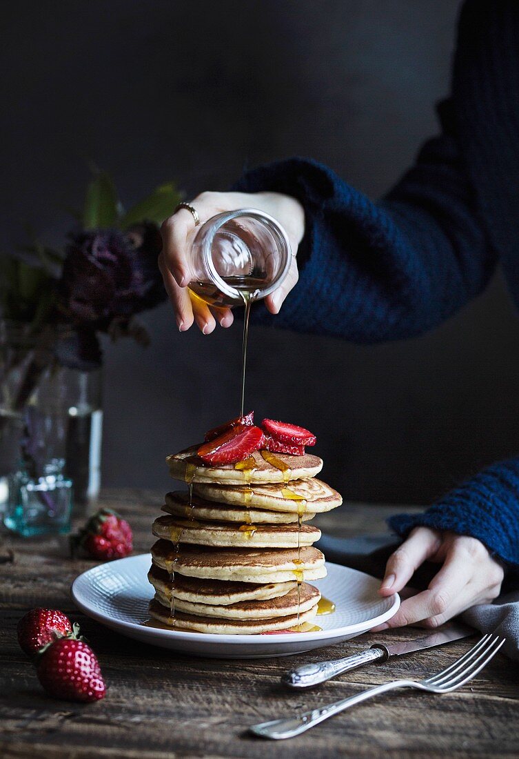 Woman pouring maple syrup on the pancakes with strawberries